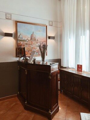 A reception desk with a painting of a cityscape, a vase with dried plants, and a sign indicating room number 94.