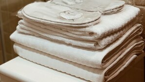 A stack of white towels on a white shelf in a bathroom with beige tiles. - Residenza Sciarra (Rome)