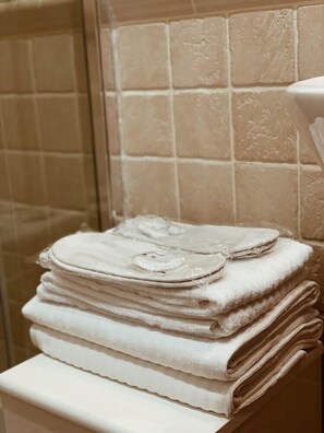 A stack of white towels on a white shelf in a bathroom with beige tiles. - Residenza Sciarra (Rome)