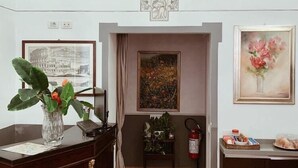 A reception area with a desk, a vase with flowers, framed artwork, and a fire extinguisher. - Residenza Sciarra (Rome)