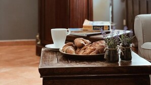 A cozy room with a wooden coffee table, a white cup, a plate of croissants, and a vase with flowers. - Residenza Sciarra (Rome)