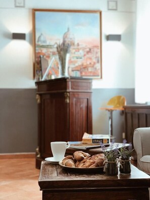 A cozy room with a wooden coffee table, a white cup, a plate of croissants, and a vase with flowers. - Residenza Sciarra (Rome)