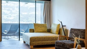 A modern bedroom with a large window, a bed with patterned bedding, a chair, and a small table with a vase. - Crystal Hotel (Fuegen)
