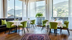 A dining area with a table set for four, green chairs, and a view of the countryside through large windows. - Crystal Hotel (Fuegen)