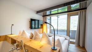 A modern hotel room with a wooden vanity, a large bed with white pillows, a mounted TV, and a window with a view of the countryside. - Crystal Hotel (Fuegen)