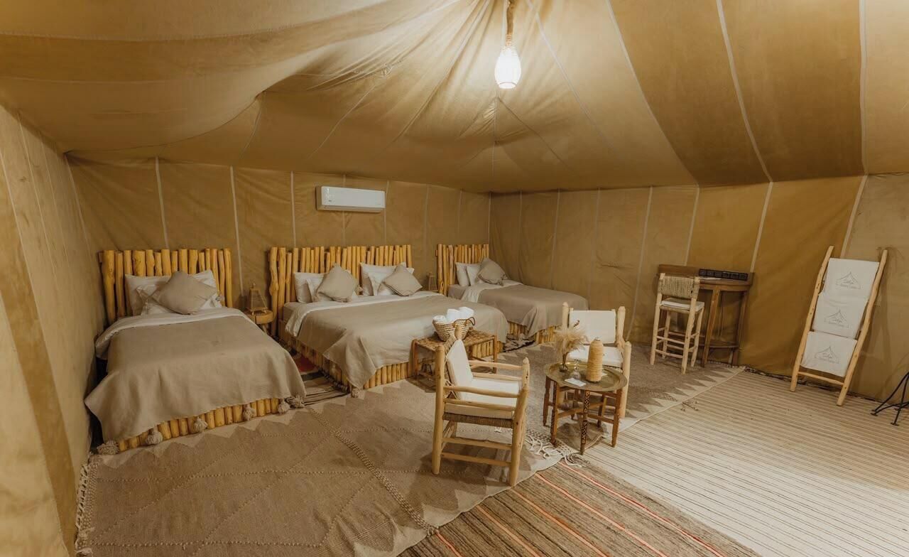 Una habitación con carpa, tres camas, una mesita y una silla.