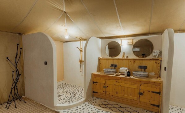 Un baño con tocador de madera, dos espejos redondos, ducha con cabezal de ducha manual y piso estampado.