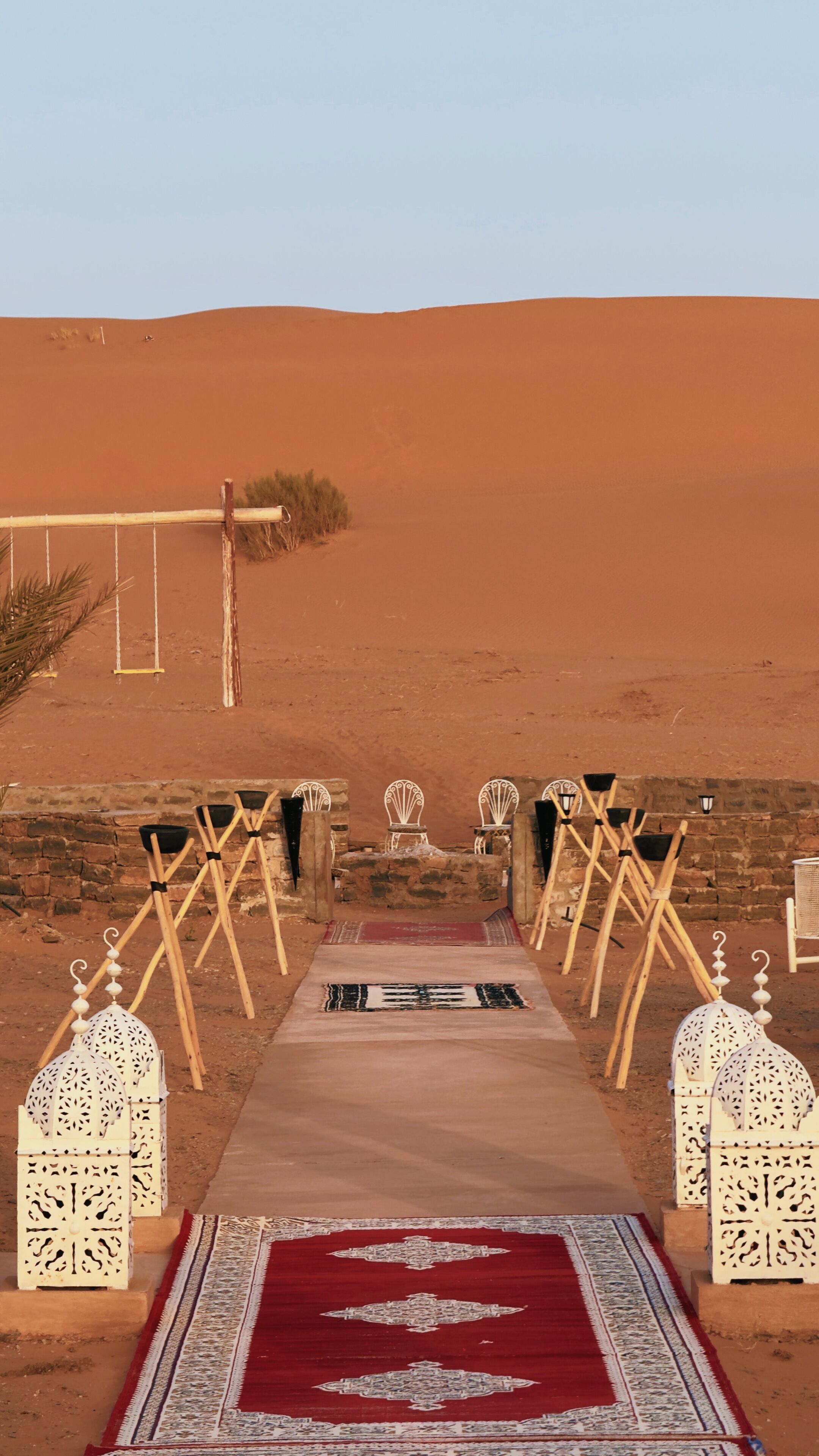 A desert setting with a pathway leading to a seating area with white chairs and lanterns.