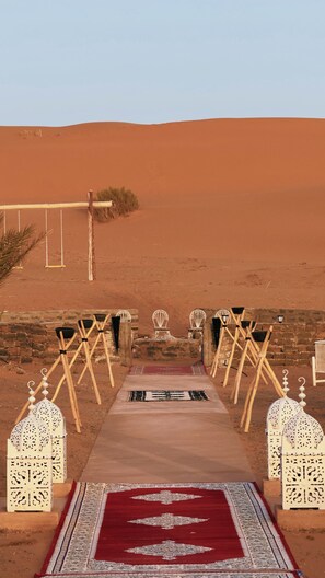 A desert setting with a pathway leading to a seating area with white chairs and lanterns. - Dihya Desert Camp (Taouz)