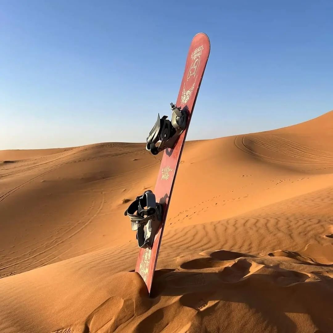 Ein Snowboard, das an einer Sanddüne anlehnt, mit blauem Himmel.