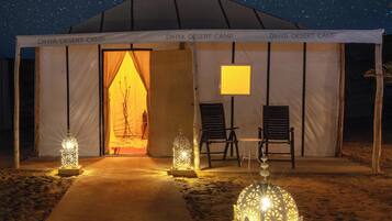 Un campamento en el desierto con la entrada de una tienda, dos sillas y faroles decorativos.