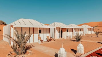 Remolque de tiendas de campaña en el desierto, cielo despejado, vegetación escasa y terreno arenoso plano.