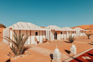 Remolque de tiendas de campaña en el desierto, cielo despejado, vegetación escasa y terreno arenoso plano.