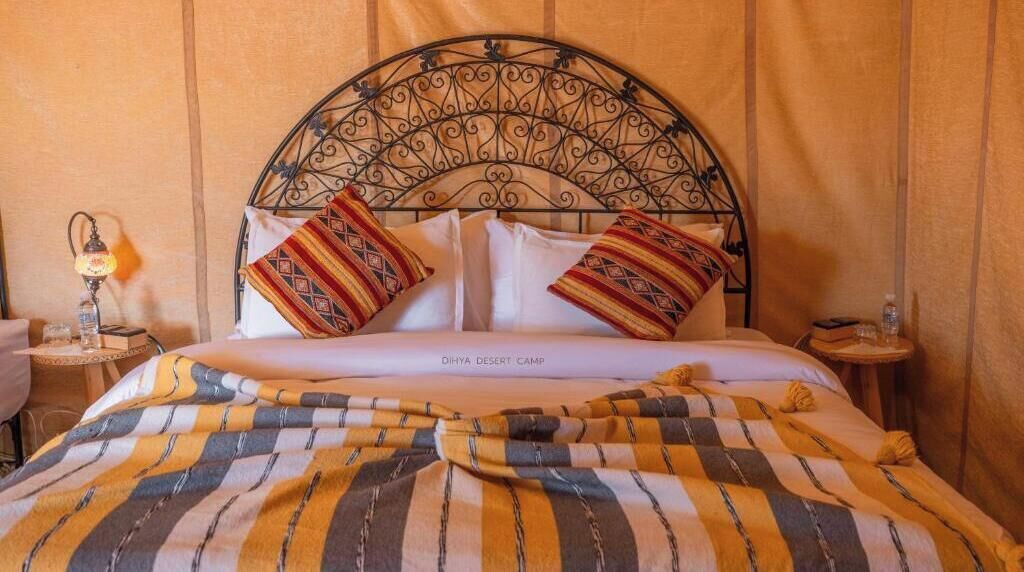 A bed with a metal headboard, two pillows, a striped blanket, and a small bedside table with a lamp.