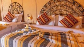 Een kamer met twee bedden, elk voorzien van gestreept beddegoed en decoratieve kussens. Er staat een klein tafeltje met een lamp en een waterfles ernaast.