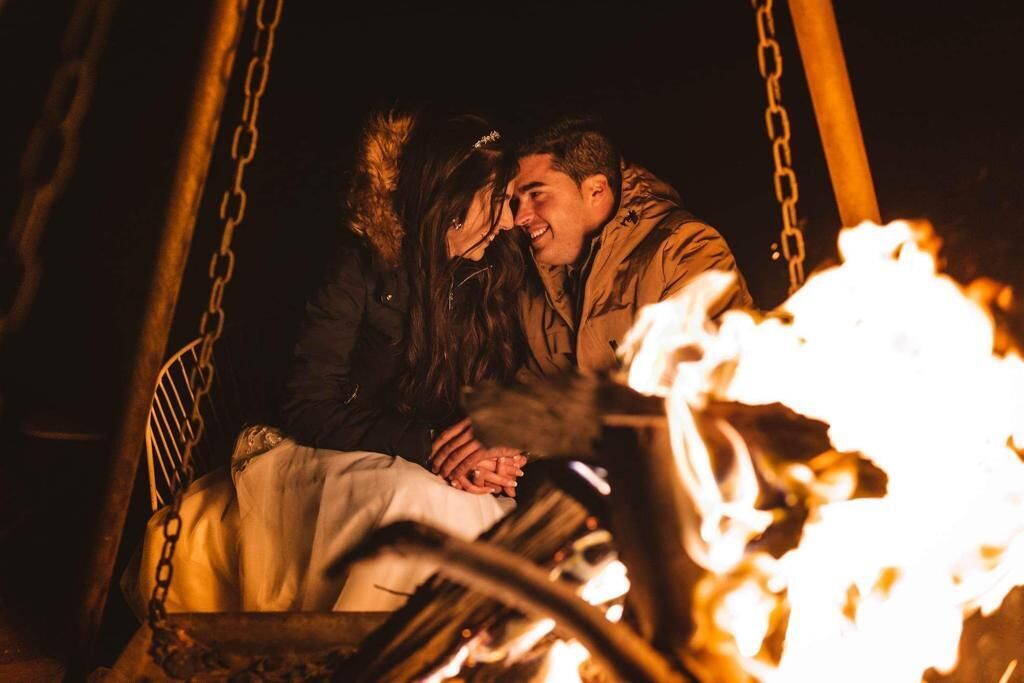 A couple sitting on a swing with a fire in the foreground.