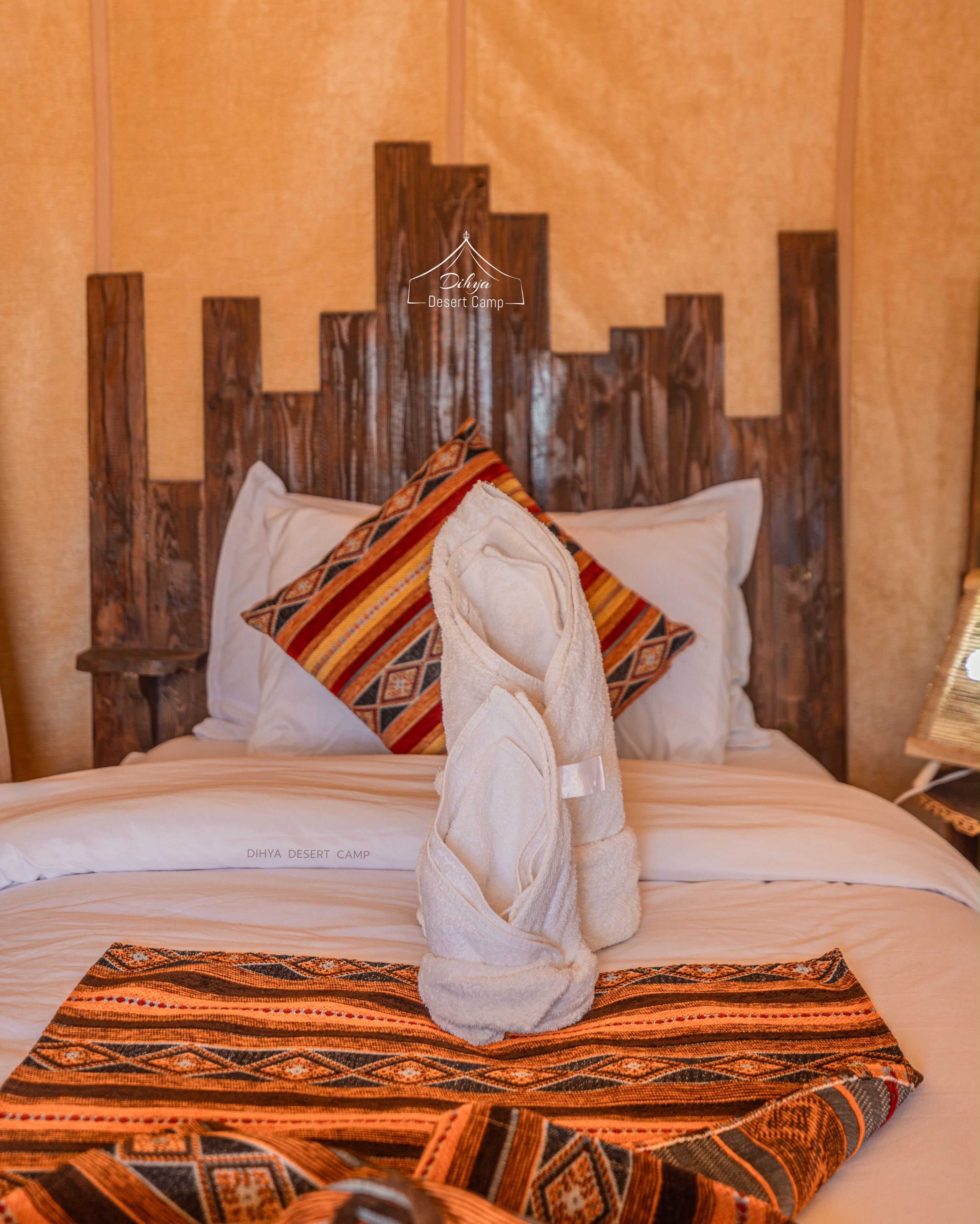 A bed with a wooden headboard, a white towel, and a patterned blanket.