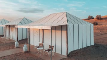 Acampamento no deserto com tendas, cada uma com um banco e uma mesa.