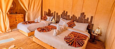 Ein Zimmer mit zwei Betten, einem Holz-Kopfteil, einem gewebten Teppich und einem Nachttisch aus Holz mit einer Lampe.