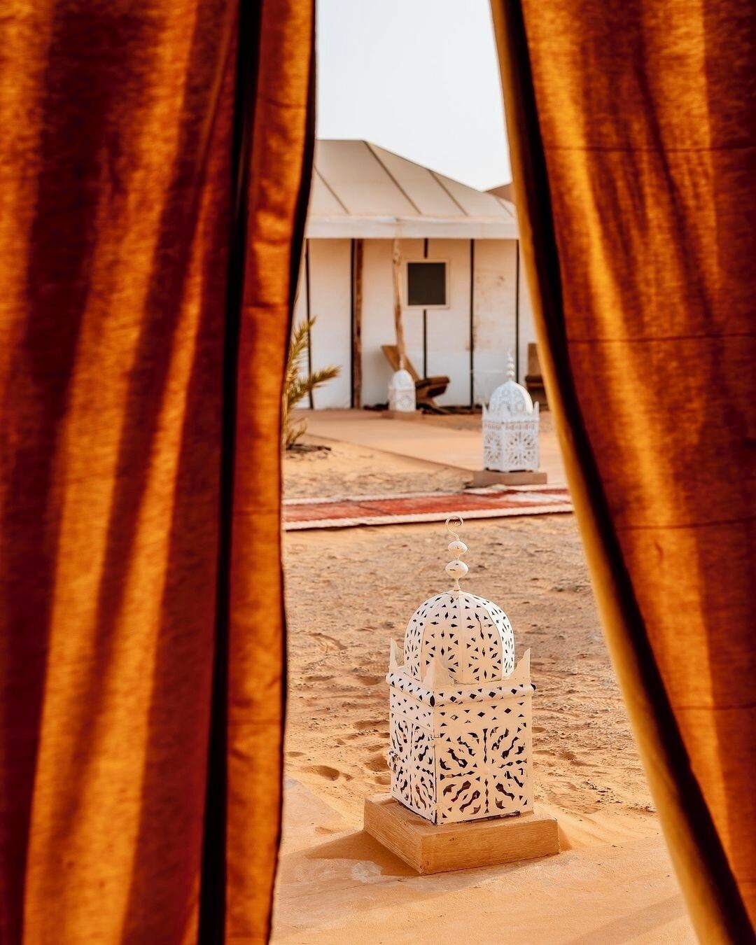 A desert scene with a white tent and a decorative lantern in the foreground.