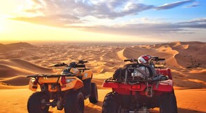 Two ATVs parked on sand dunes with a desert landscape in the background. - Dihya Desert Camp (Taouz)