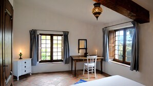 Une chambre à coucher comprenant un lit, un bureau, une chaise, une commode, deux fenêtres avec des rideaux et un luminaire suspendu.