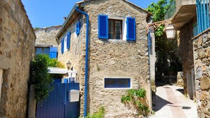Une étroite ruelle pavée, avec une porte bleue, des bâtiments en pierre et un ciel d’un bleu limpide.