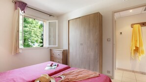 Ein Schlafzimmer mit zwei Betten, einem Kleiderschrank, einem Fenster mit Vorhängen und einem Handtuch an der Wand.