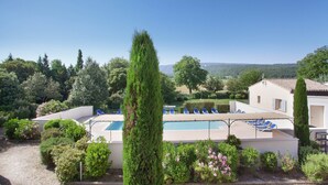 Ein Poolbereich mit Liegestühlen, umgeben von Grünpflanzen und Blick auf die Landschaft.