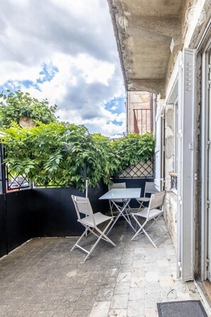 An outdoor patio with a table and chairs, a black wall, and a view of a building with a metal gate.