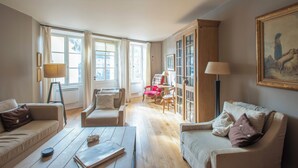 A spacious living room with a wooden floor, two sofas, a coffee table, a red chair, and a large window with curtains. - Charming house in Burgundy (Saint-Gengoux-le-national)