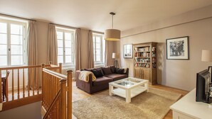 A spacious living room with a brown sofa, a glass coffee table, a wooden bookshelf, and a large window with curtains. - Charming house in Burgundy (Saint-Gengoux-le-national)