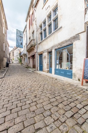 Una calle adoquinada flanqueada por edificios, uno con toldo azul y un cartel.