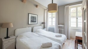 A hotel room with two beds, a nightstand with a lamp, a framed picture on the wall, and a window with curtains. - Charming house in Burgundy (Saint-Gengoux-le-national)