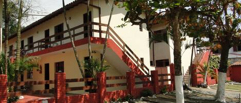 A two-story building with a red brick base and beige upper floors, surrounded by trees and a paved area.