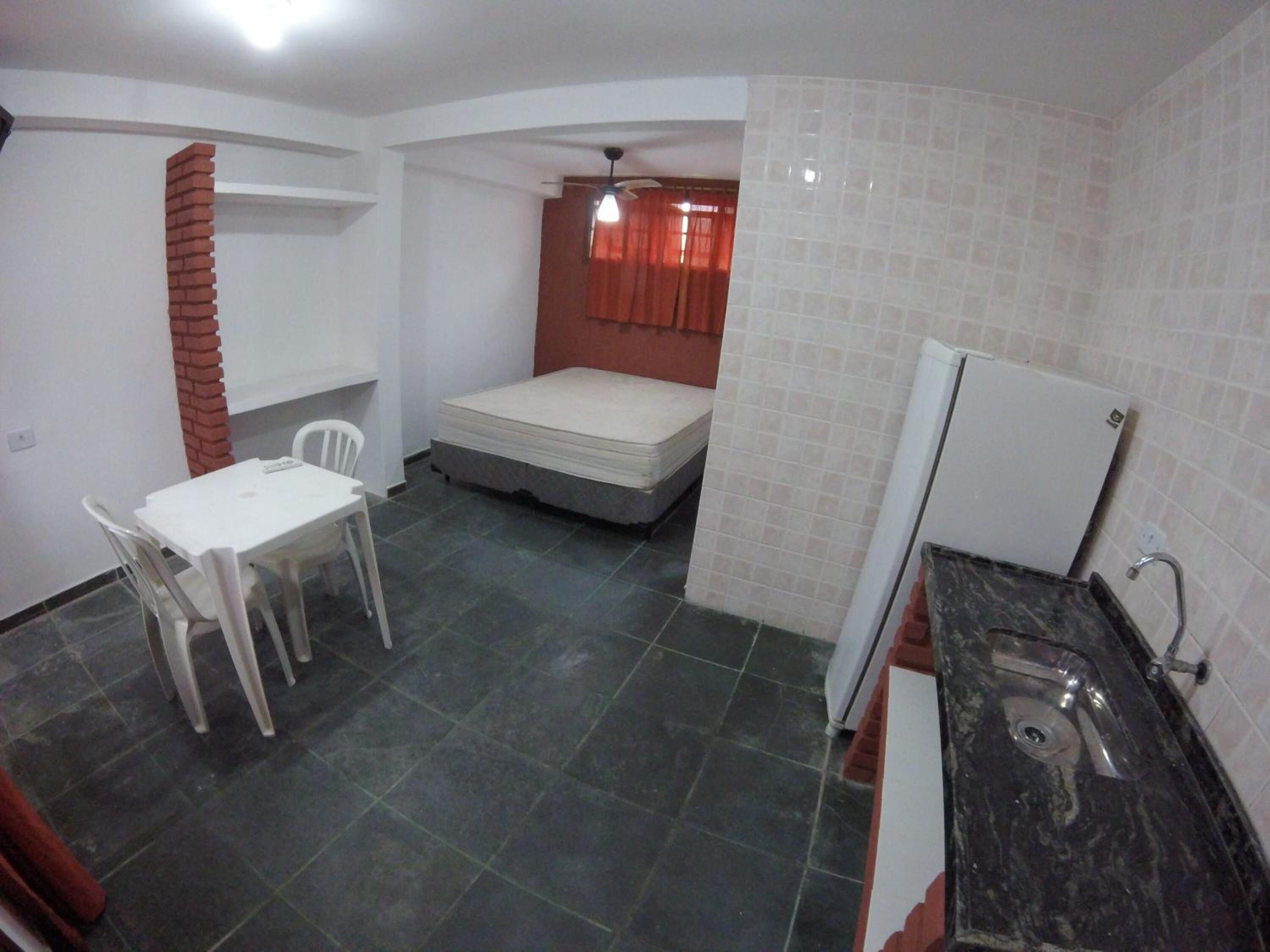 Habitación pequeña con cama, una mesita con sillas, kitchenette y suelo de baldosas.