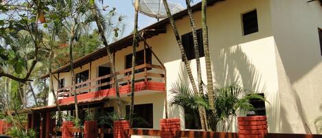 A two-story building with a balcony, surrounded by palm trees and a brick fence.