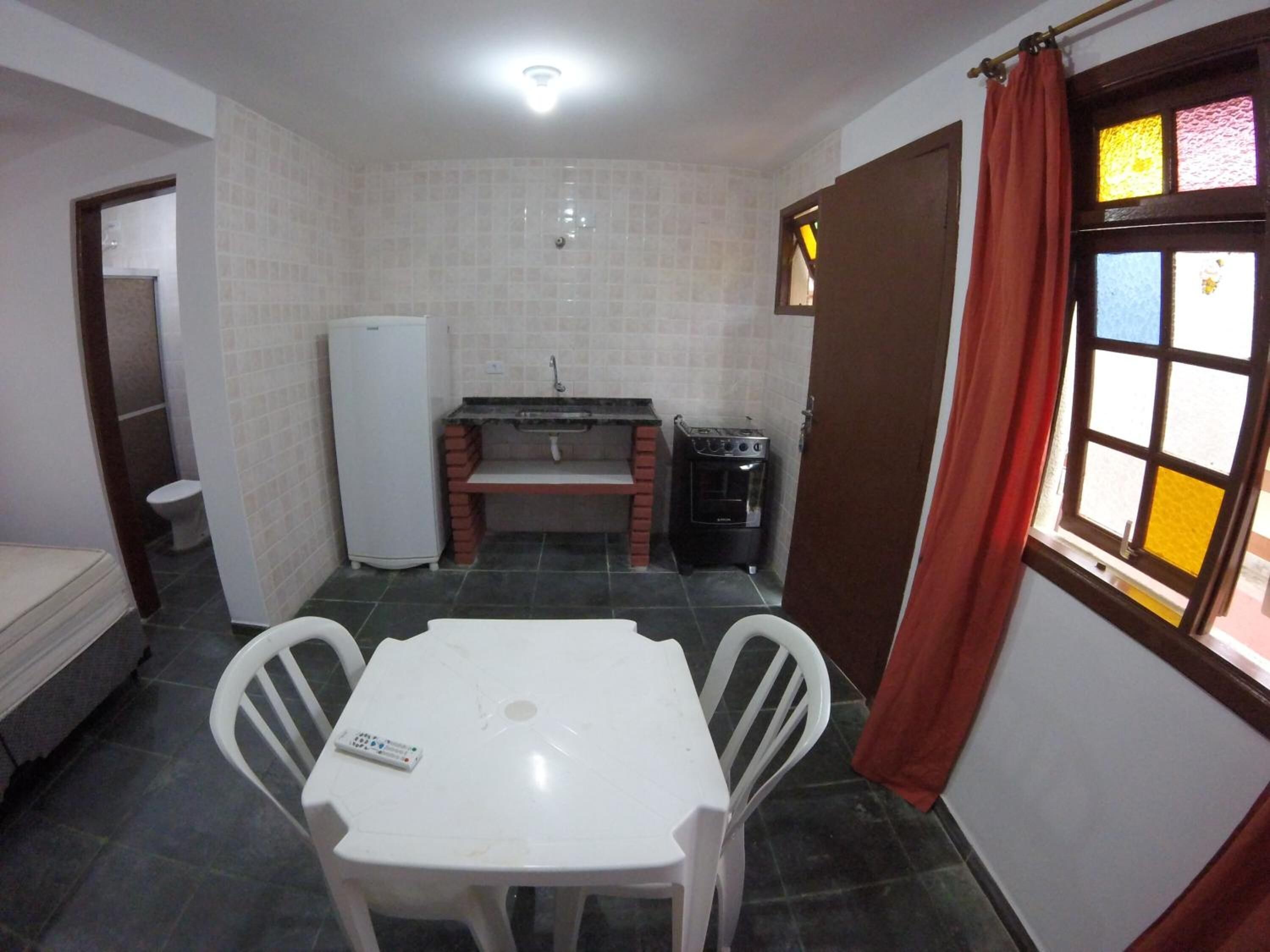 A small kitchen with a refrigerator, stove, and sink. There is a table with two chairs and a window with curtains.