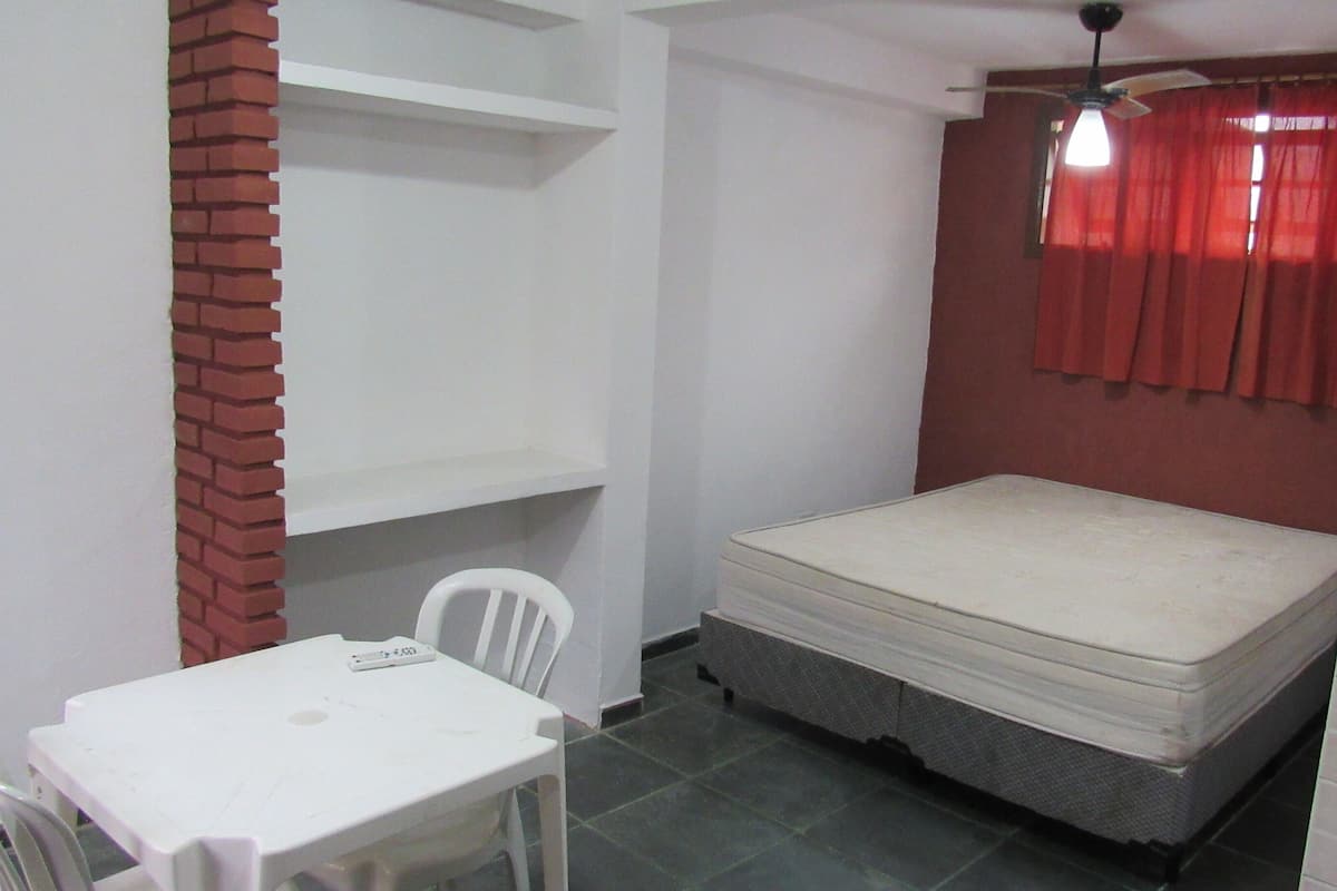 Una habitación pequeña con una cama individual, una mesa blanca, una silla blanca y una cortina roja.