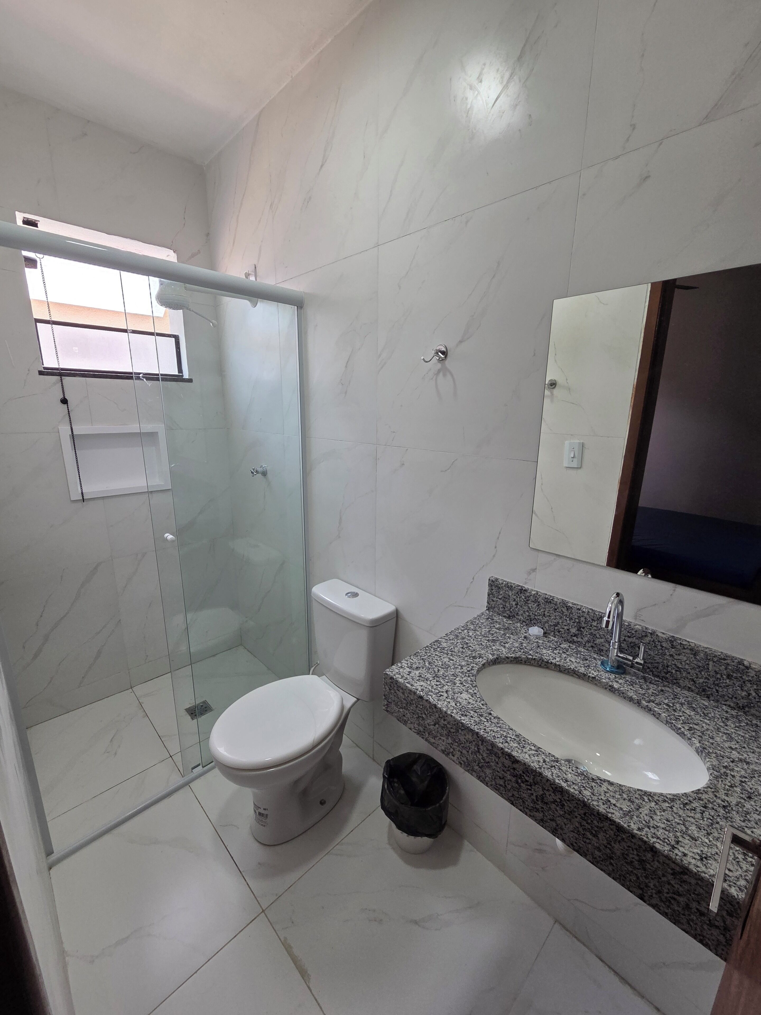 A bathroom with a glass shower enclosure, a toilet, and a granite countertop sink.