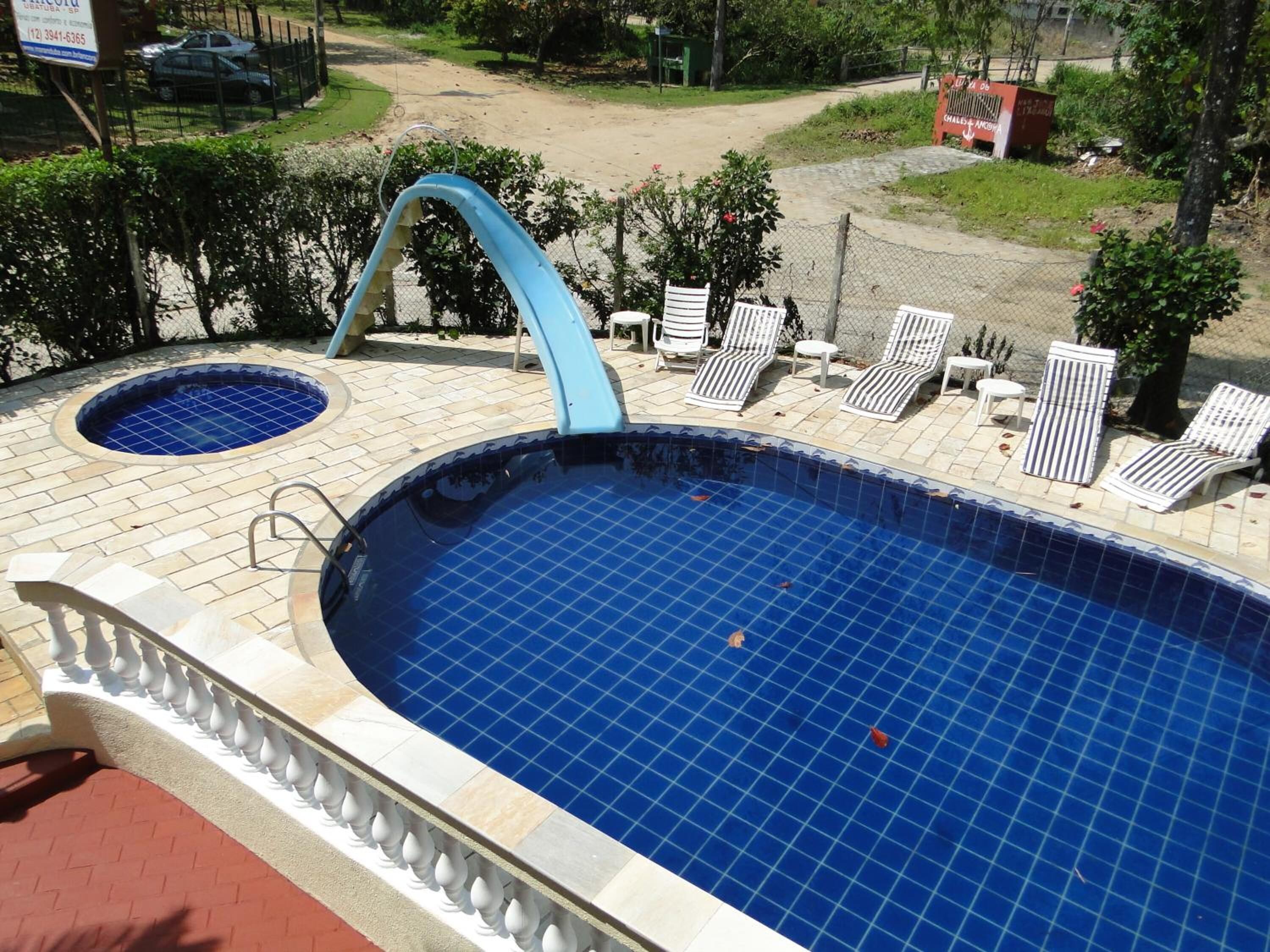 A swimming pool with a blue tiled interior, a small adjacent hot tub, and several lounge chairs around the pool area.