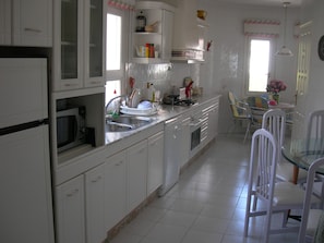 Een keuken met witte kasten, een magnetron, een spoelbak en een eethoek met stoelen en een tafel.