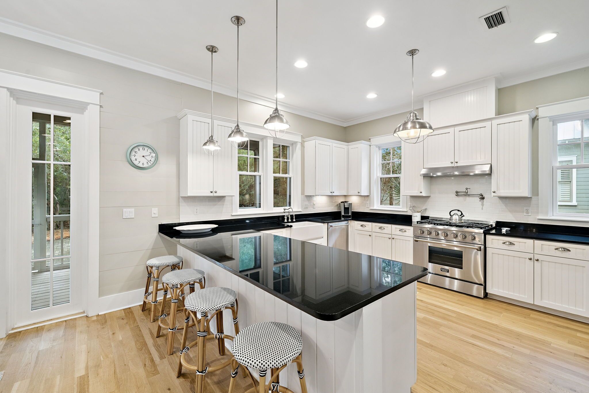 A modern kitchen with white cabinetry, a large island with bar stools, stainless steel appliances, and pendant lighting.