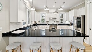 A modern kitchen with white cabinetry, a black countertop, and three bar stools with patterned seats. - Pet-Friendly WaterColor Retreat | Pool Spring '27 | Cart & Bikes (Santa Rosa Beach, Florida)