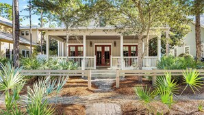 A two-story house with a covered porch, a front door, and a small front yard with plants. - Pet-Friendly WaterColor Retreat | Pool Spring '27 | Cart & Bikes (Santa Rosa Beach, Florida)