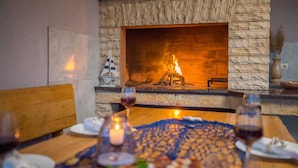 A dining table with plates, glasses, and a candle, set against a stone fireplace with a fire.