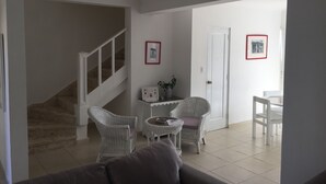 A living room with a staircase, white wicker chairs, a small table, and a sofa.