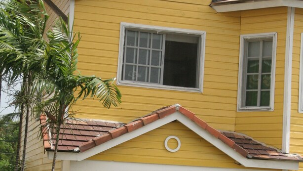 A yellow two-story house with a red-tiled roof, white trim, and a front porch.