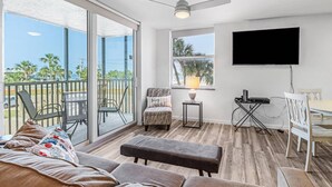 A spacious living area with a balcony, a flat-screen TV, and a seating area with a sofa and chairs. - Beach & Tennis 1207 (Bonita Springs)