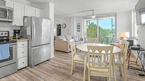 A modern kitchen with stainless steel appliances, a dining area with a round table and chairs, and a balcony with a view of the ocean. - Beach & Tennis 1207 (Bonita Springs)